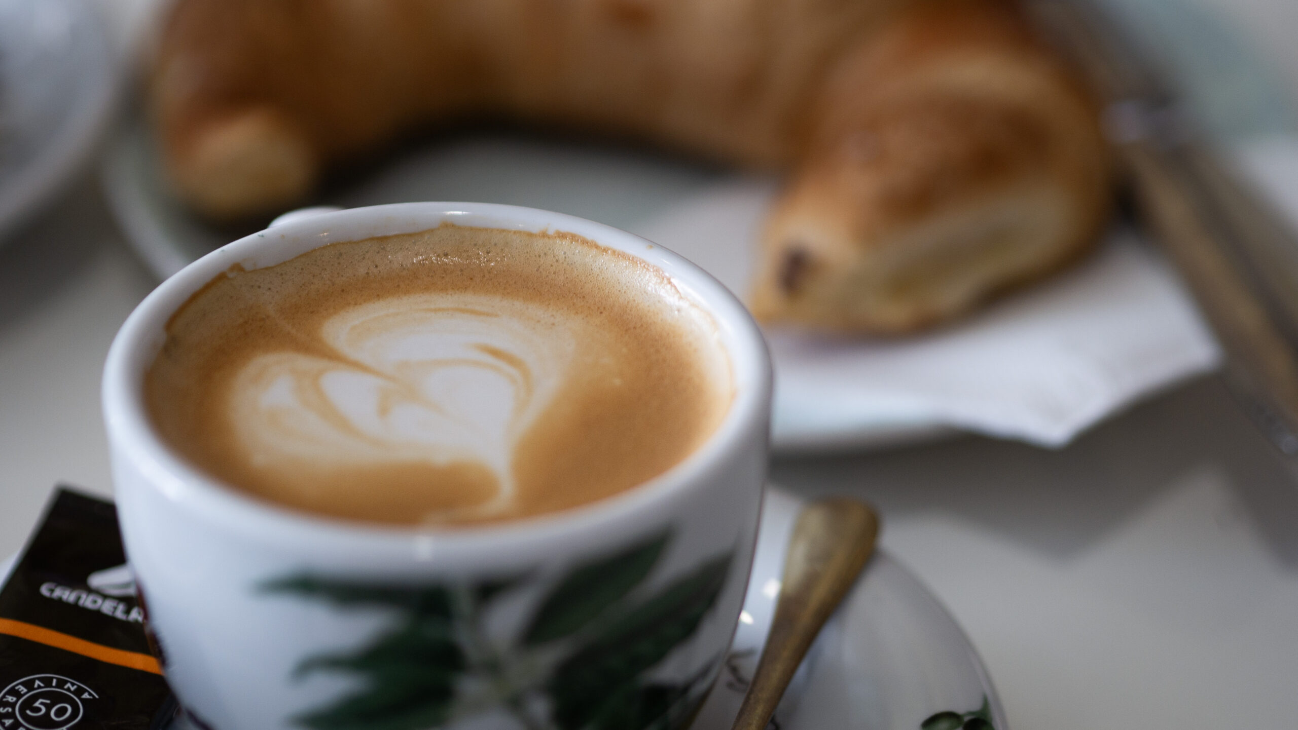 Café con leche cremoso en taza de café Candelas. Fondo de croissant.